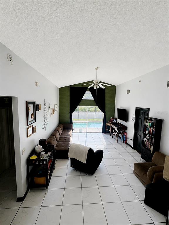A living room with white tile floors, a long brown sofa, and a pool view — 324 CASTERTON CIRCLE, DAVENPORT, FL