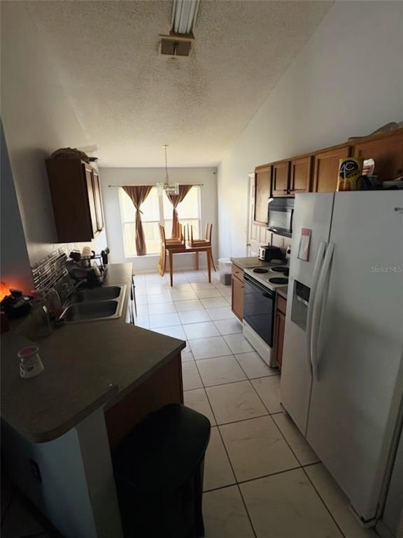 A kitchen with wood cabinets, white appliances, and tile flooring leads to a dining area — 324 CASTERTON CIRCLE, DAVENPORT, FL