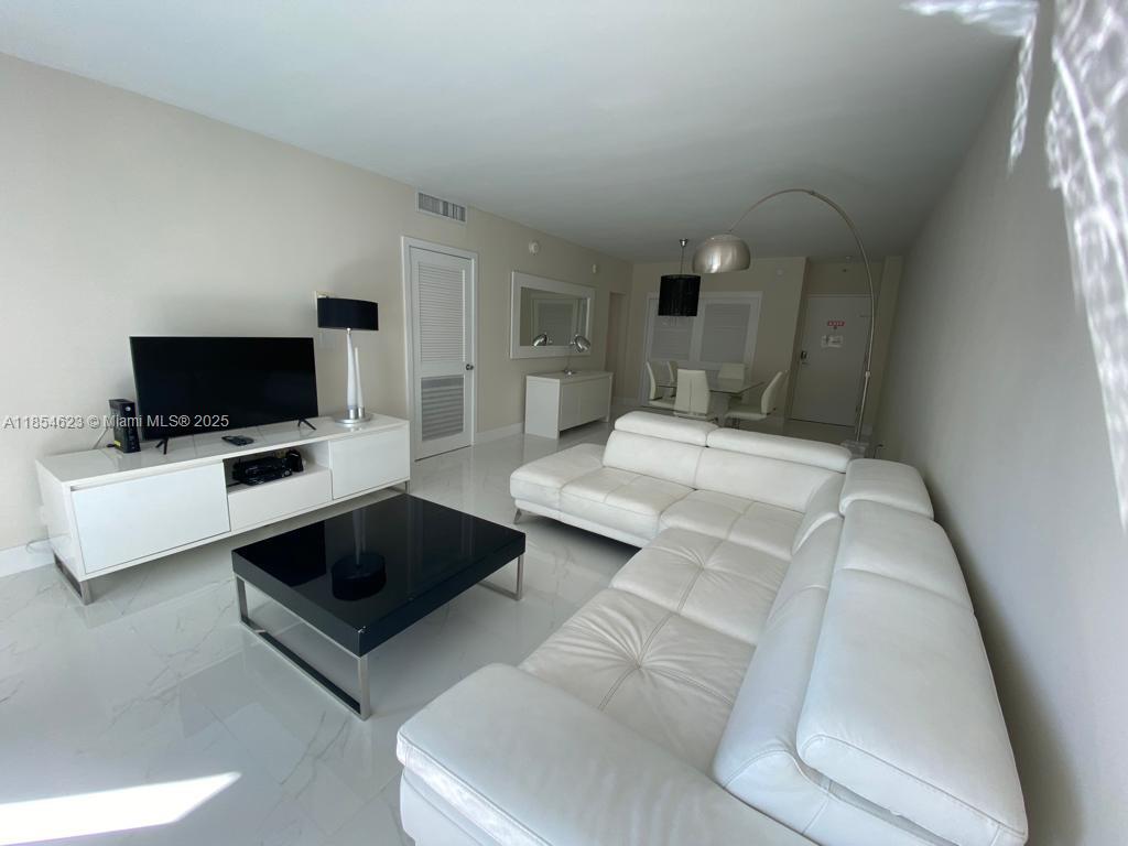 A living room features a white sectional sofa, a black coffee table, and white tile flooring — 4001 S Ocean Dr # 10F, Hollywood FL 33019, HOLLYWOOD, FL
