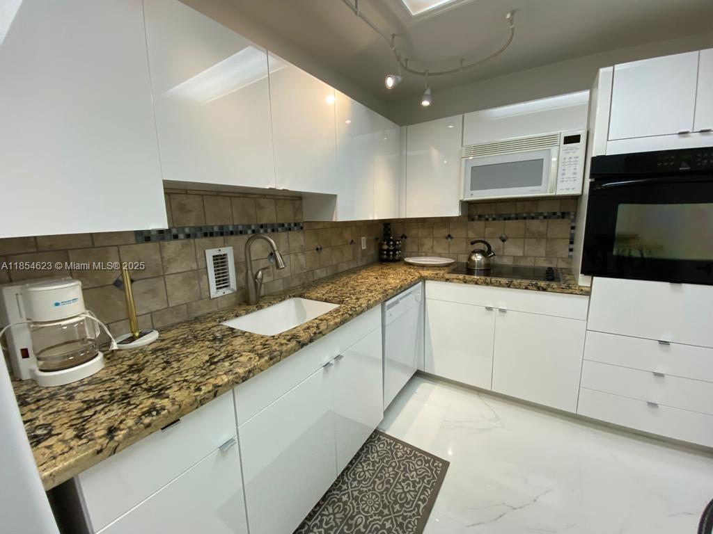 A kitchen features white glossy cabinets, granite countertops, a tiled backsplash, and stainless steel appliances — 4001 S Ocean Dr # 10F, Hollywood FL 33019, HOLLYWOOD, FL