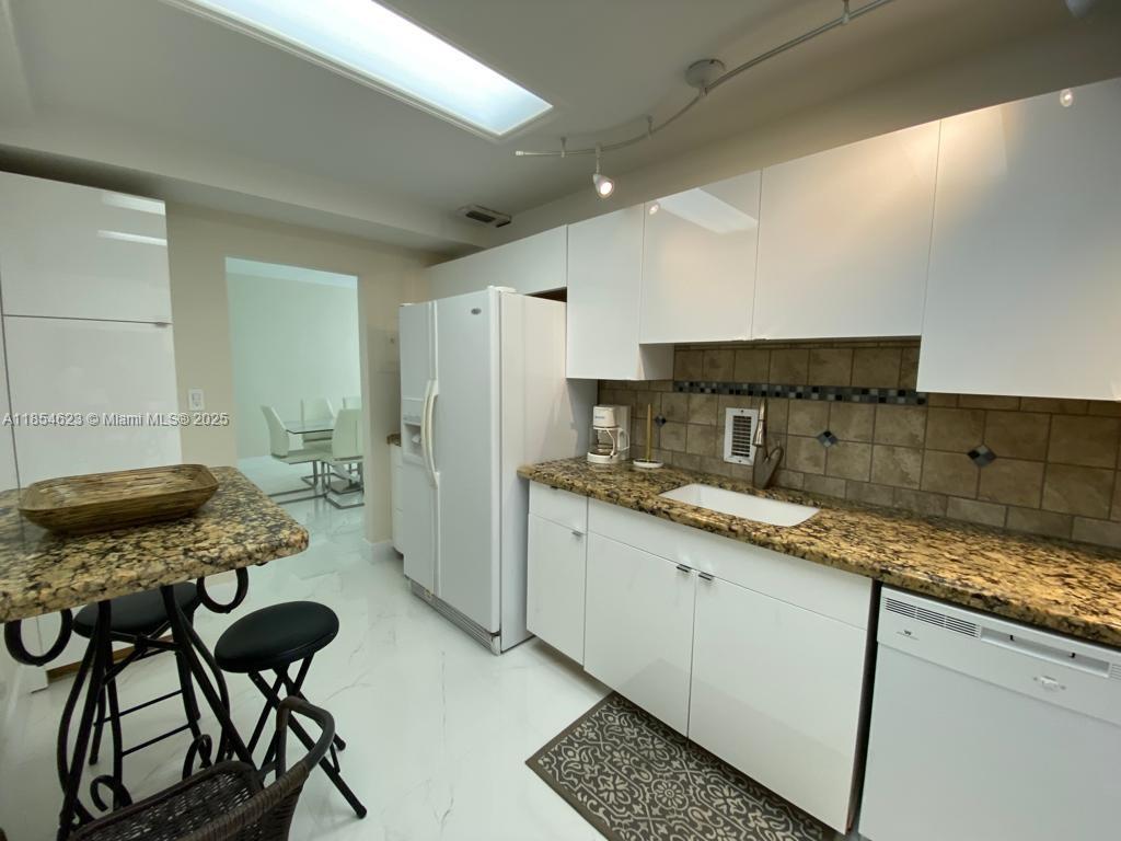 A kitchen features white cabinets, granite countertops, a white refrigerator, and a breakfast bar — 4001 S Ocean Dr # 10F, Hollywood FL 33019, HOLLYWOOD, FL