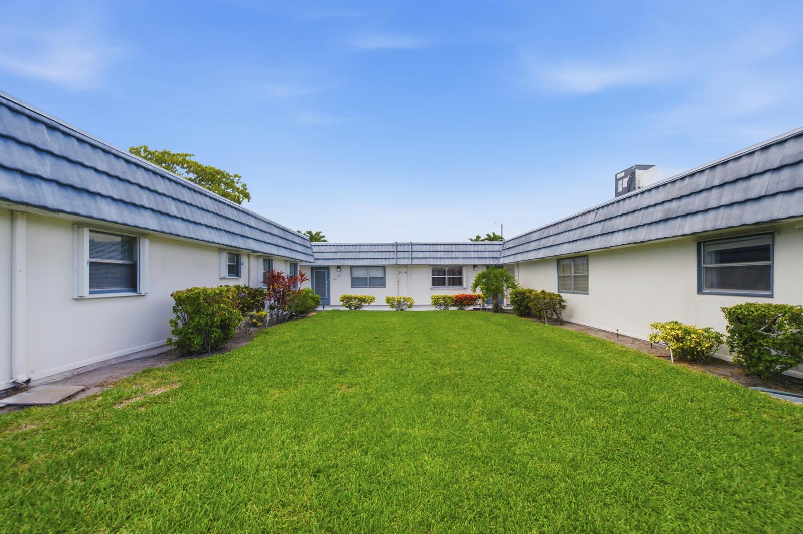 A grassy courtyard sits between two single-story residential buildings with blue mansard-style roofs — 30 Waterford B, Delray Beach FL 33446, DELRAY BEACH, FL