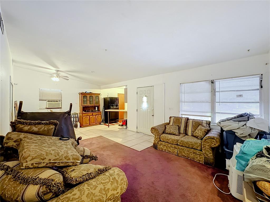 A living room with carpeted flooring, a patterned sofa, and an adjacent tiled kitchen area — 202 N 39TH STREET, FORT PIERCE, FL
