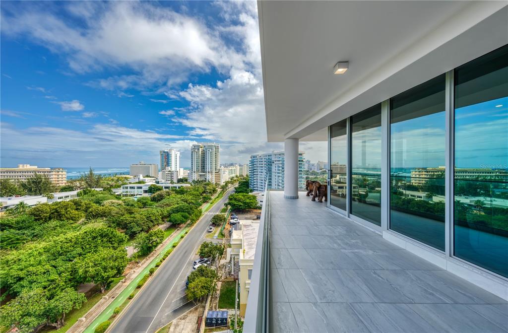 A modern balcony with gray tile flooring overlooks a coastal city, trees, and the ocean — 540 AVE. DE LA CONSTITUCION UNIT 1101, SAN JUAN, PR
