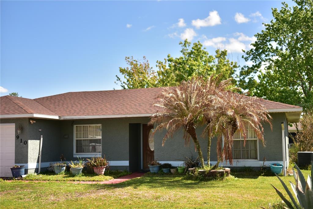 A single-story house with gray stucco siding, a brown roof, and a palm tree out front — 910 LOUVRE COURT, KISSIMMEE, FL