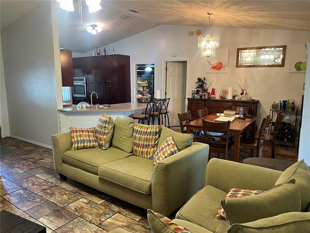 A living room with green sofas opens to a kitchen with dark cabinets and dining area — 910 LOUVRE COURT, KISSIMMEE, FL