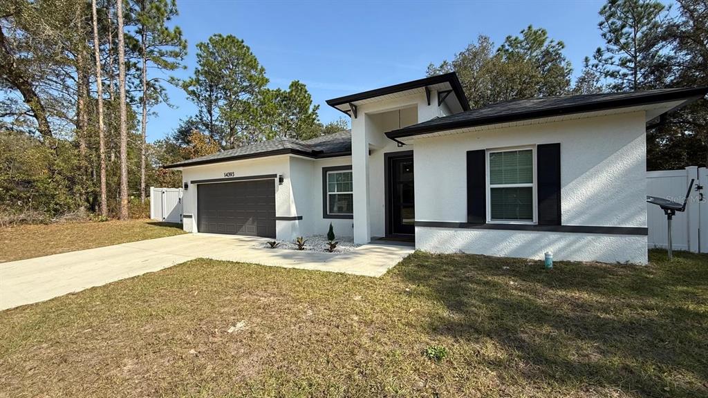 A single-story house with white stucco walls, a dark garage door, and a front entrance — 14393 SW 79TH TERRACE, OCALA, FL