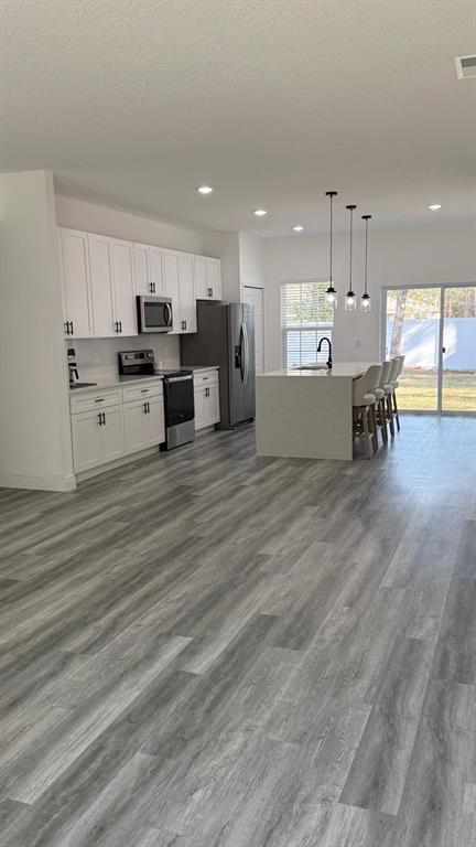 A modern kitchen features white cabinetry, stainless steel appliances, a center island, and wood-look flooring — 14393 SW 79TH TERRACE, OCALA, FL
