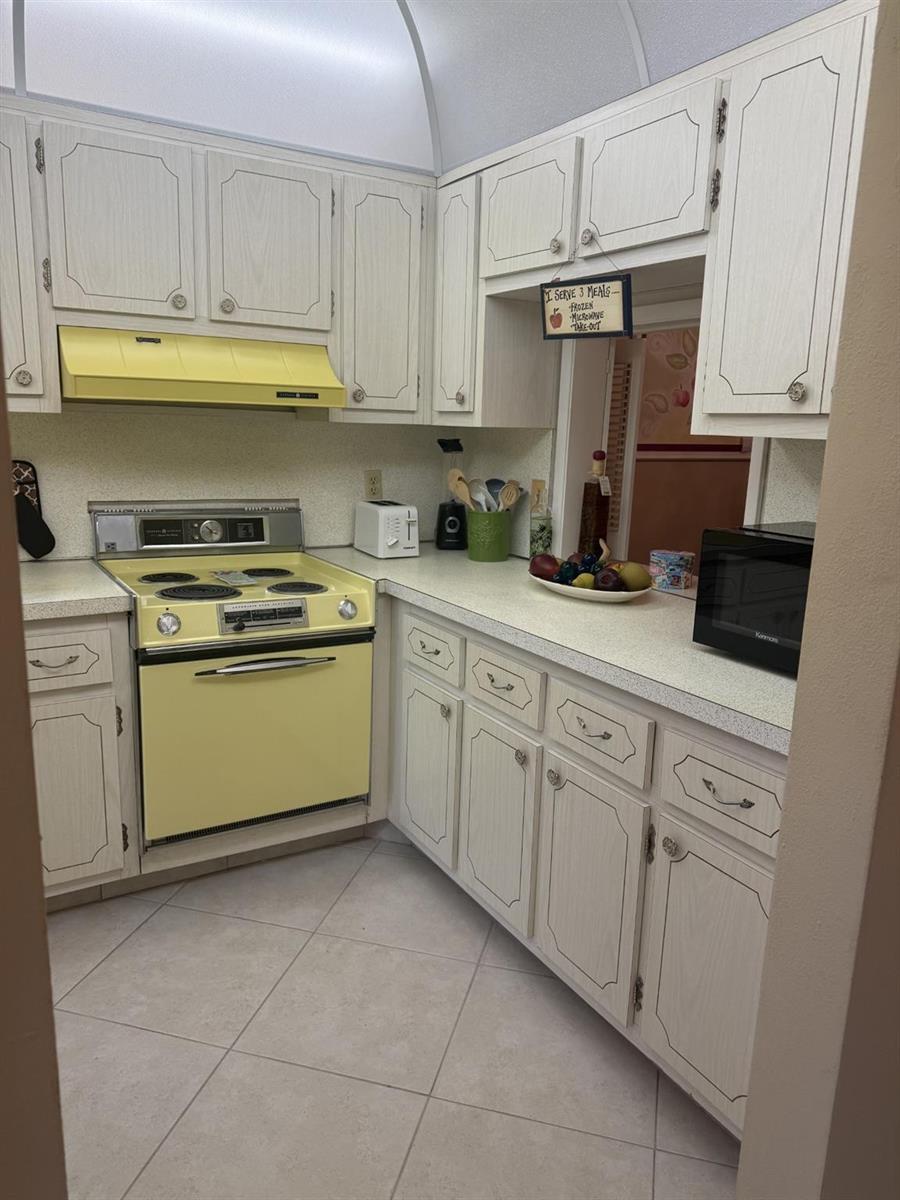 A kitchen features light wood cabinets, a yellow stove and range hood, and tile flooring — 2050 NE 39th Street # 211w, Lighthouse Point FL 33064, LIGHTHOUSE POINT, FL