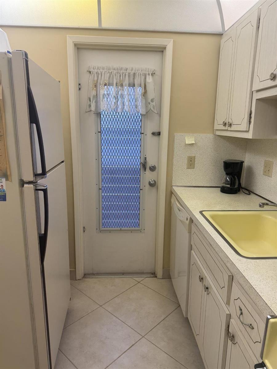 A kitchen features white appliances, light-colored cabinets, a yellow sink, and a glass-paneled exterior door — 2050 NE 39th Street # 211w, Lighthouse Point FL 33064, LIGHTHOUSE POINT, FL