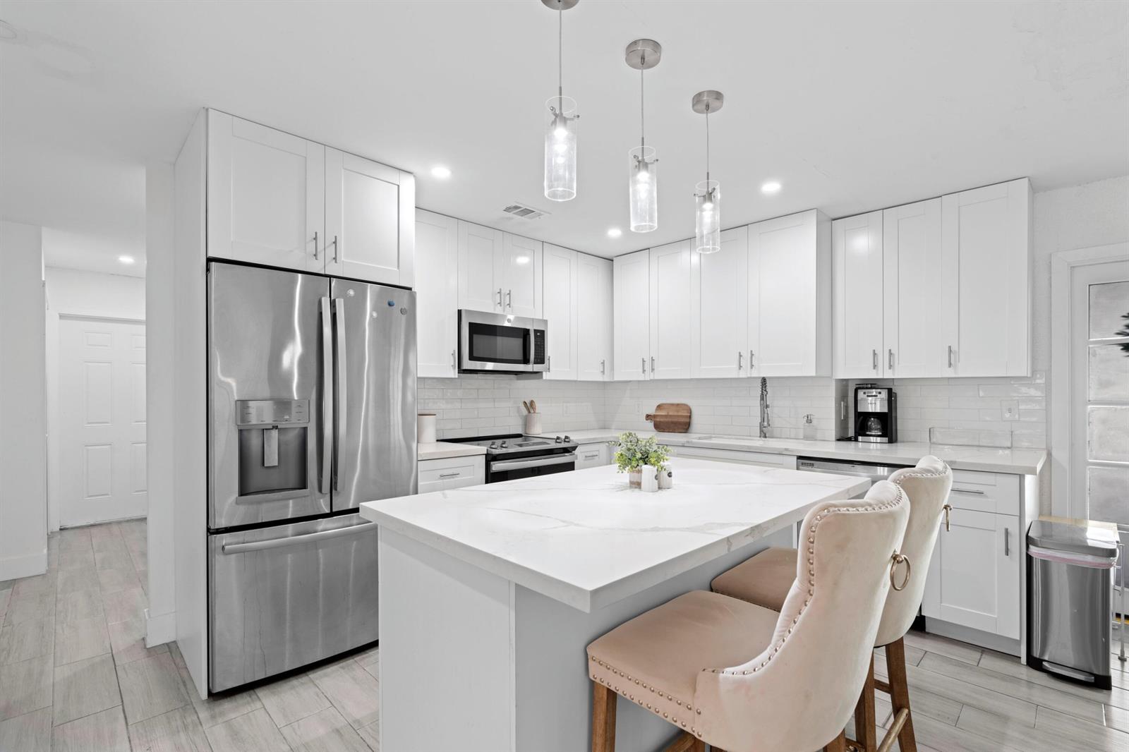 A modern kitchen features white cabinetry, stainless steel appliances, and a central marble-topped island — 5285 Sunrise Boulevard, Delray Beach FL 33484, DELRAY BEACH, FL