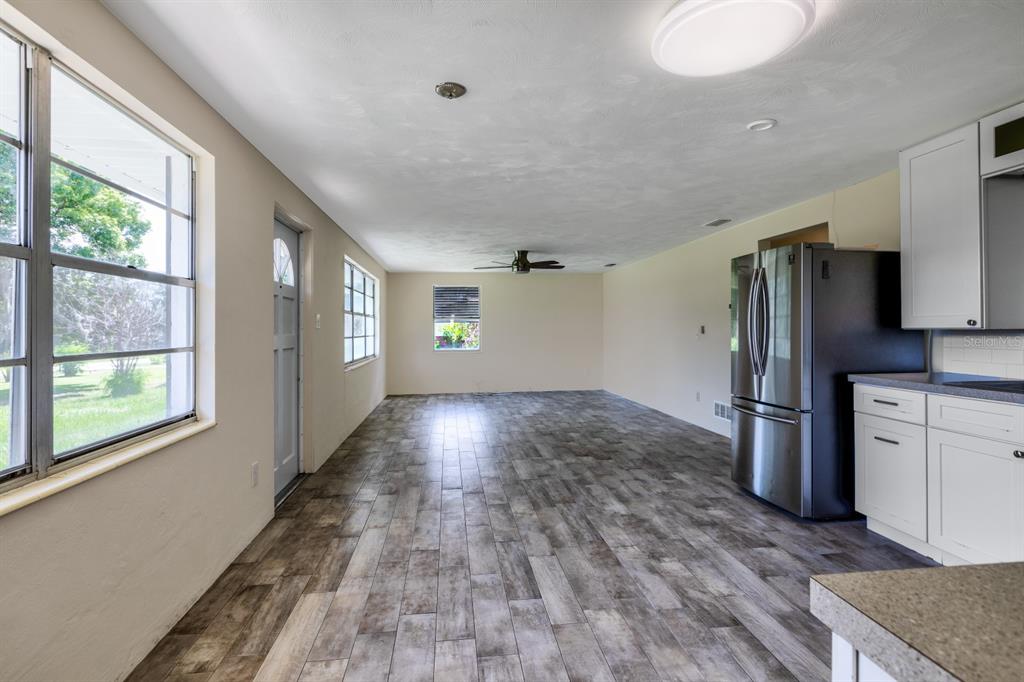 A kitchen and living area with wood-look tile flooring, white cabinets, and a stainless refrigerator — 5222 EAGLES NEST ROAD, FRUITLAND PARK, FL