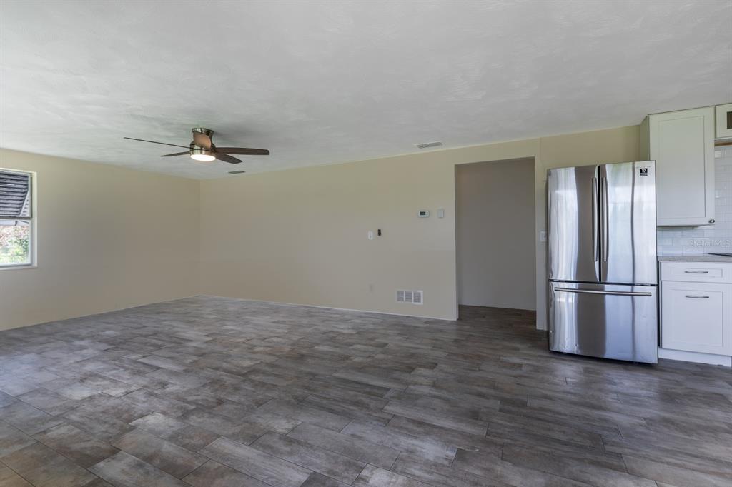 A spacious room with wood-look tile flooring, a ceiling fan, and a stainless steel refrigerator — 5222 EAGLES NEST ROAD, FRUITLAND PARK, FL