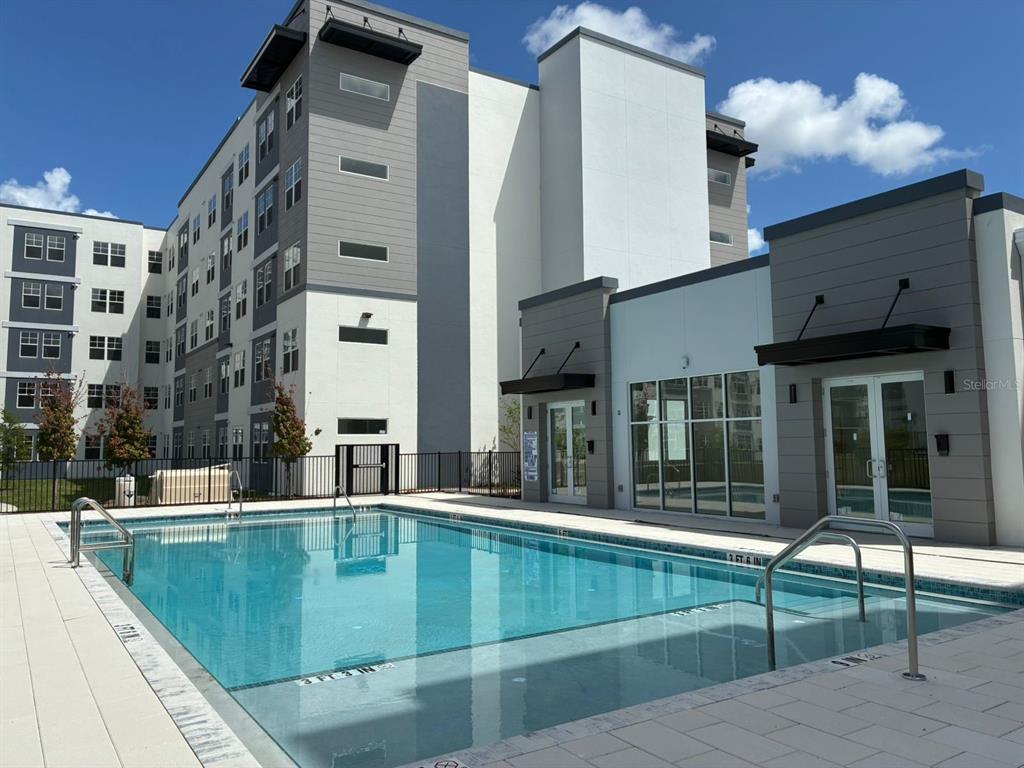 A rectangular swimming pool sits in front of a modern multi-story apartment building — 5587 MILLENIA PARK BOULEVARD UNIT 318, ORLANDO, FL