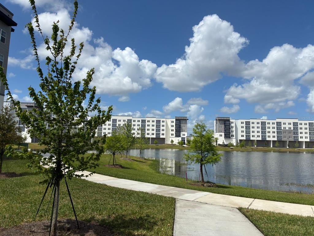 A paved walkway leads past a pond toward a large multi-story apartment complex — 5587 MILLENIA PARK BOULEVARD UNIT 318, ORLANDO, FL