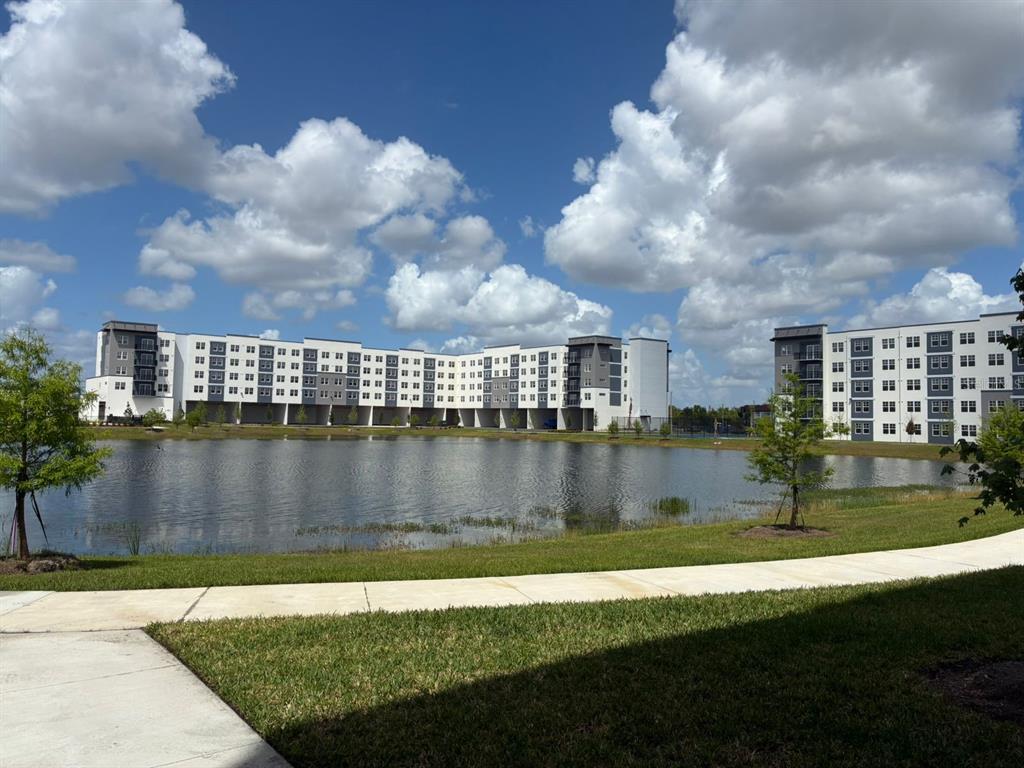 A multi-story apartment complex sits behind a pond with a paved walkway in the foreground — 5587 MILLENIA PARK BOULEVARD UNIT 318, ORLANDO, FL
