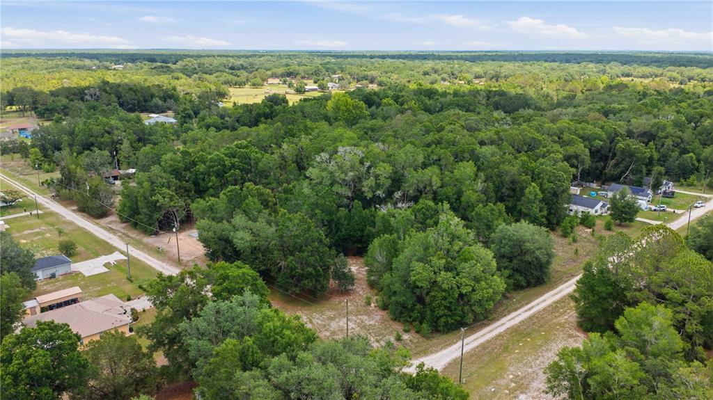 An aerial view shows a wooded lot surrounded by residential houses and dirt roads — SW 131ST TERRACE, DUNNELLON, FL