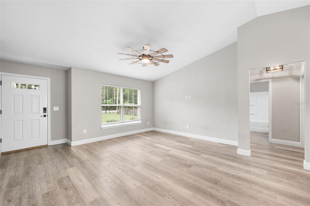 A bright living room features light wood-look flooring, gray walls, a ceiling fan, and windows — 6771 CHERRY ROAD, OCALA, FL