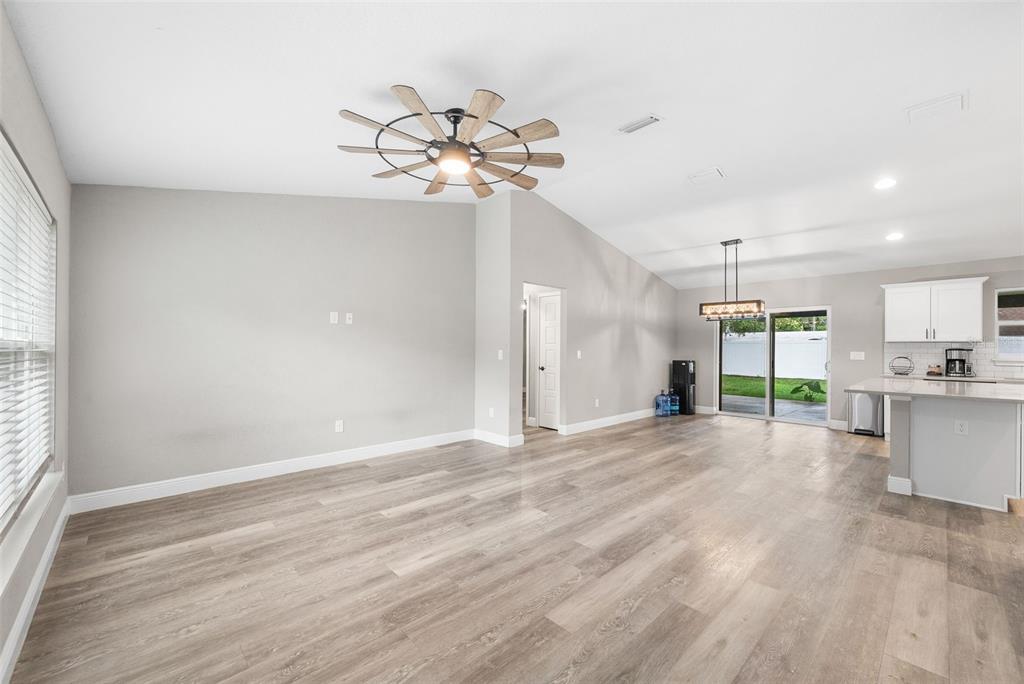 A spacious living area with light wood-look flooring, a vaulted ceiling, and an open kitchen — 6771 CHERRY ROAD, OCALA, FL