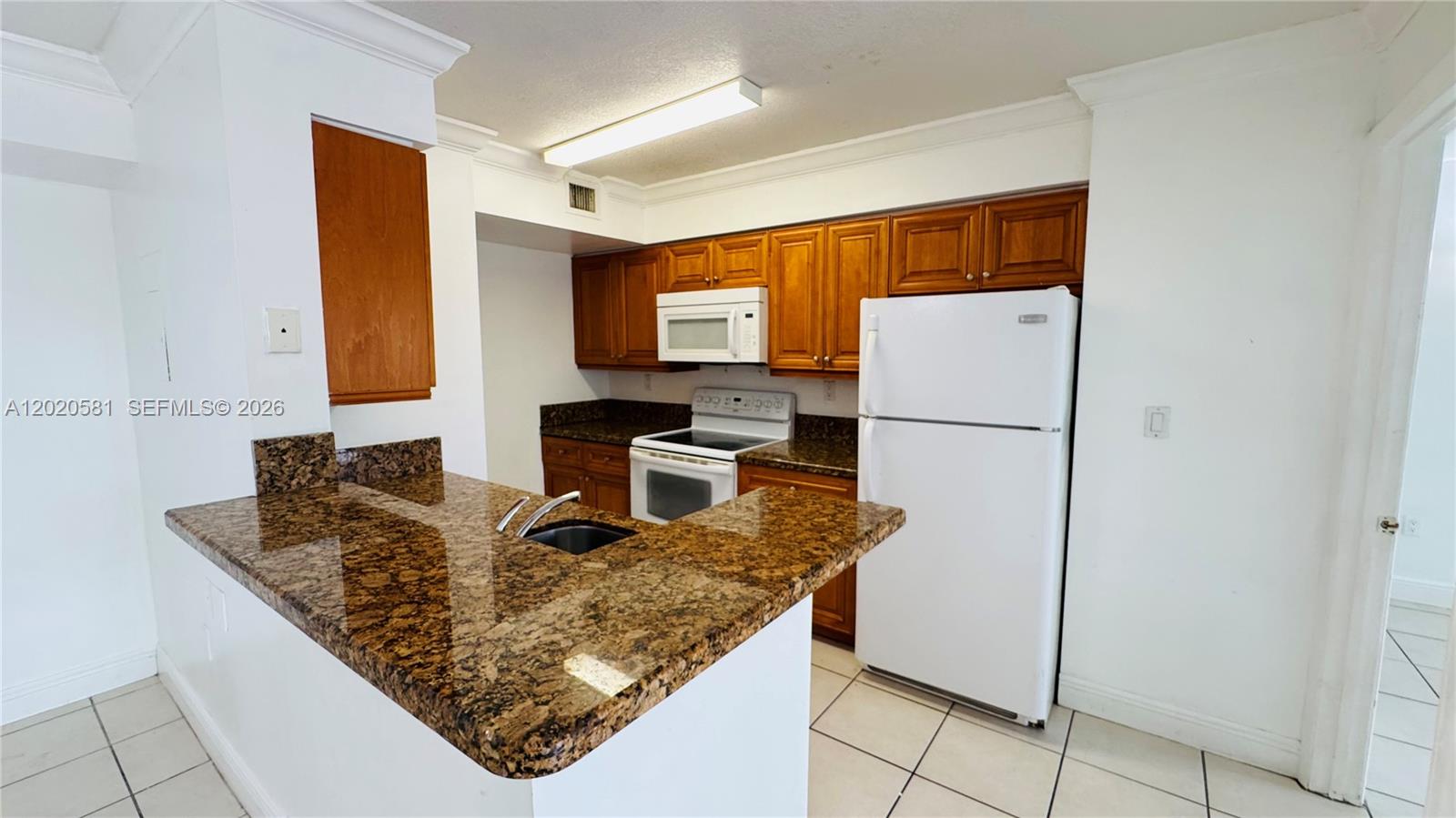 A dining area with tile floors opens to a kitchen featuring wood cabinets and appliances — 15221 SW 80th St # 406, Miami FL 33193, MIAMI, FL