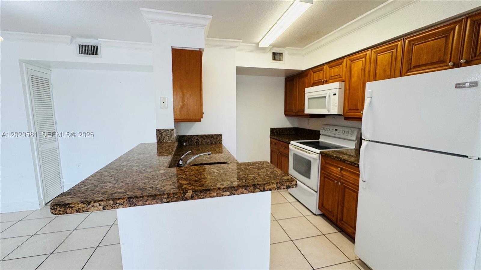 A kitchen features brown granite countertops, wooden cabinets, and white appliances — 15221 SW 80th St # 406, Miami FL 33193, MIAMI, FL