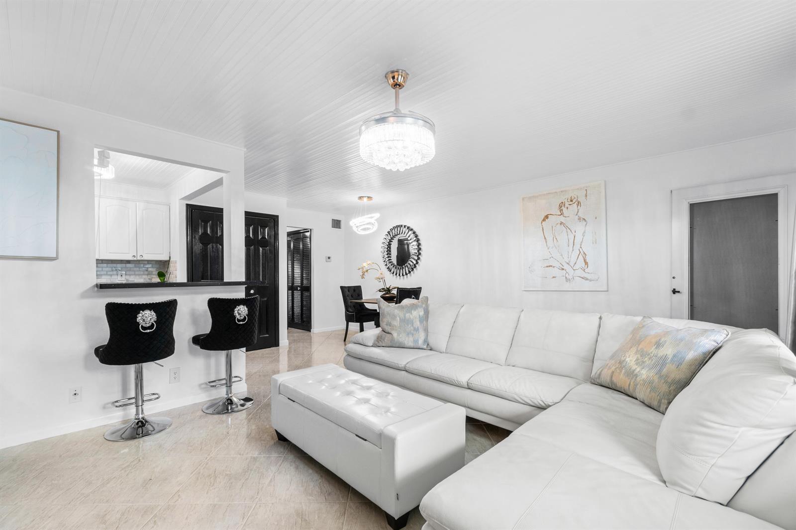 A white living room features a sectional sofa, a tufted ottoman, and a breakfast bar — 340 Horizons W # 102, Boynton Beach FL 33435, BOYNTON BEACH, FL