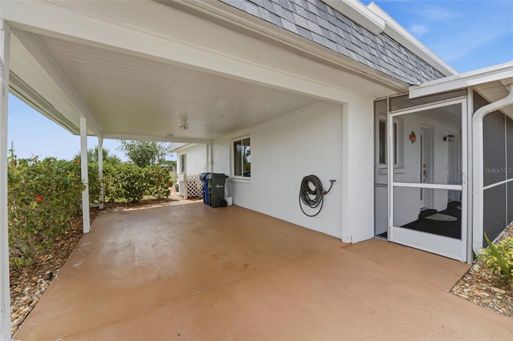 A concrete carport sits beside a white house with a screened-in entryway — 690 CIRCLEWOOD DRIVE UNIT W8, VENICE, FL