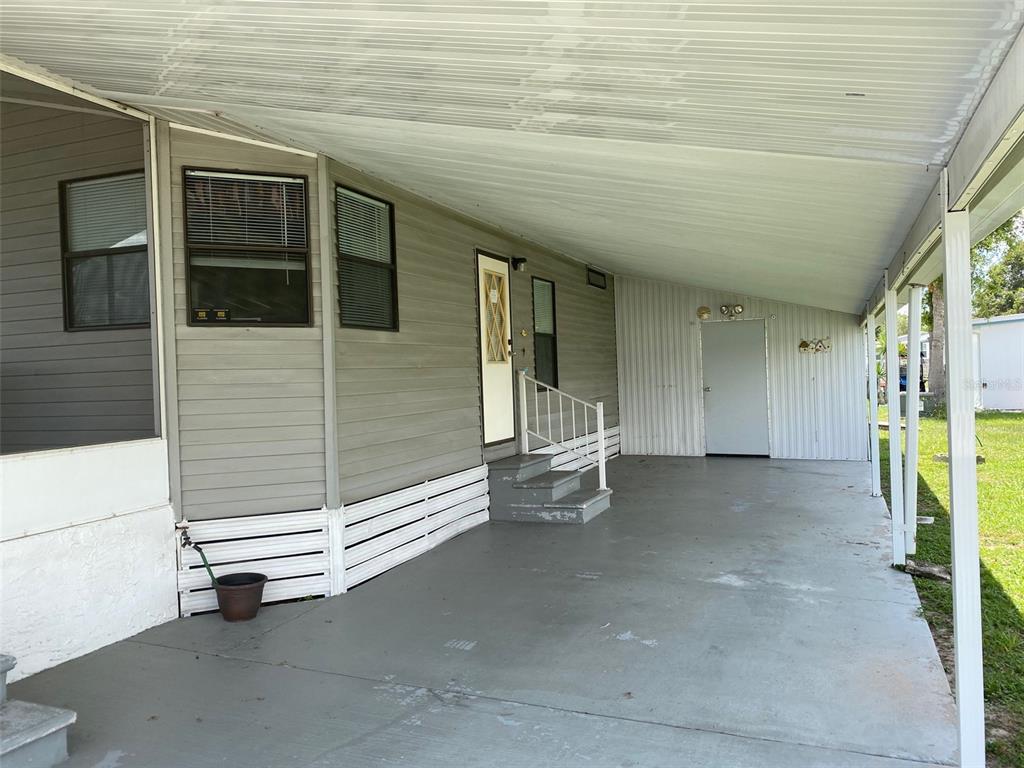 A mobile home exterior features a covered carport, concrete patio, and a small staircase — 38210 WILLIAMS AIRE STREET, DADE CITY, FL