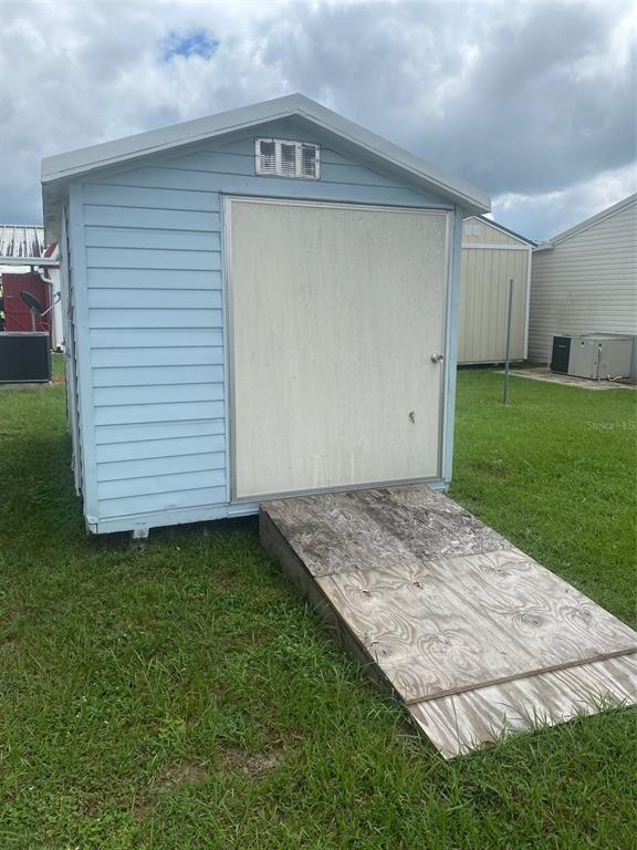 A light blue storage shed with a wooden ramp sits on a grassy lawn — 38210 WILLIAMS AIRE STREET, DADE CITY, FL