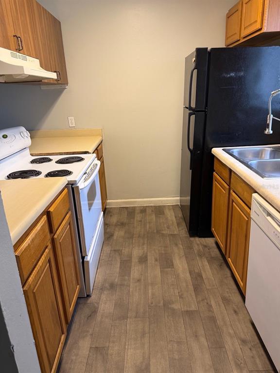 A narrow galley kitchen features wood cabinets, white appliances, and wood-look flooring — 105 CORY LANE, WINTER SPRINGS, FL