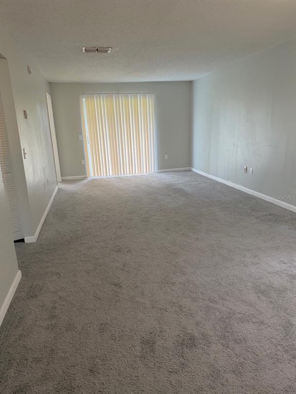 An empty living room features light gray walls, neutral carpeting, and a sliding glass door — 105 CORY LANE, WINTER SPRINGS, FL