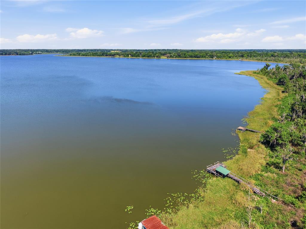 An aerial view shows a lake with two wooden docks extending from a grassy shoreline — 3980 SE 183RD AVENUE ROAD, OCKLAWAHA, FL