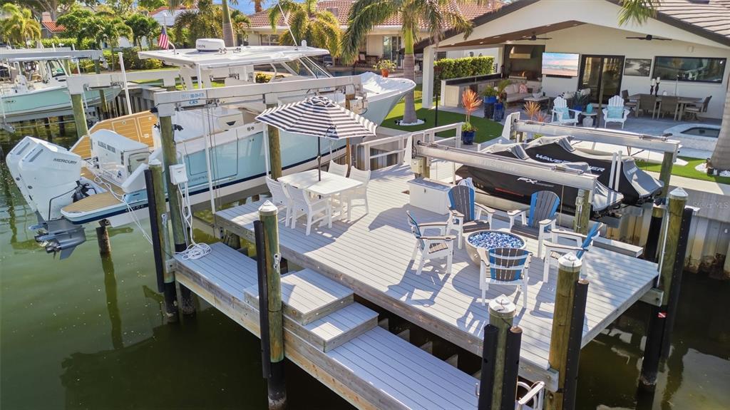 A wooden boat dock features a dining set, lounge chairs, a fire pit, and boat lifts — 2022 HAWAII AVENUE NE, ST PETERSBURG, FL