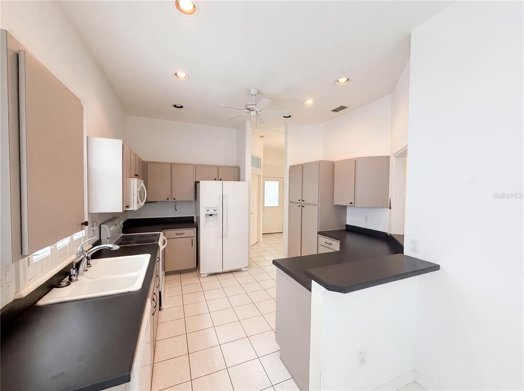 A kitchen features white tile floors, light-colored cabinets, black countertops, and a white refrigerator — 3319 NEWBLISS CIRCLE, ORMOND BEACH, FL