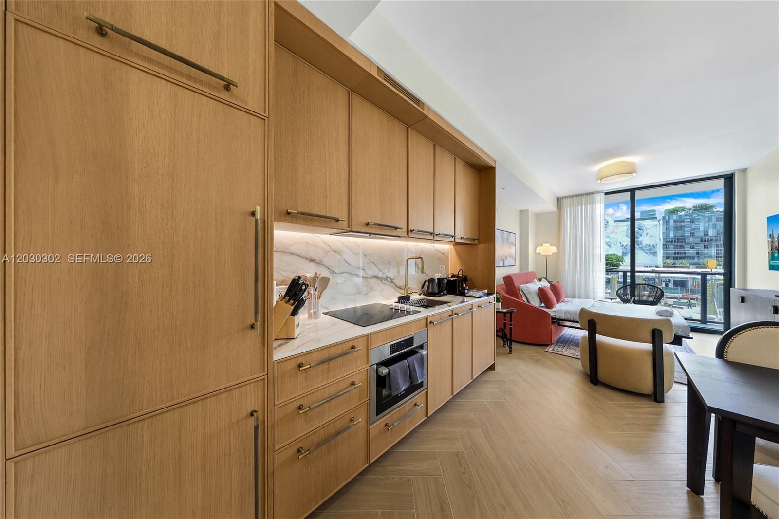 A modern kitchen with light wood cabinetry and marble backsplash opens into a living area — 2700 NW 2nd Ave # 218, Miami FL 33127, MIAMI, FL