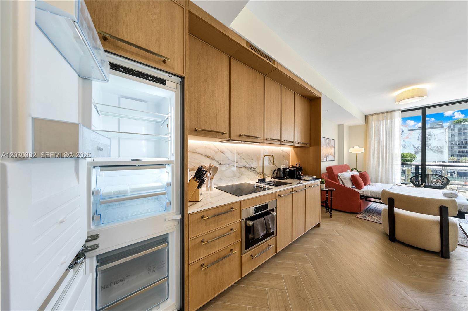 A modern kitchen with light wood cabinetry and marble backsplash opens into a living area — 2700 NW 2nd Ave # 218, Miami FL 33127, MIAMI, FL