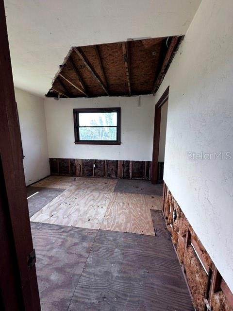 An unfinished room features exposed ceiling rafters, plywood flooring, and wall studs with visible insulation — 16540 WISTERIA DRIVE, FORT MYERS, FL