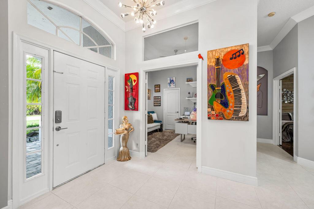 A bright entryway features white tile floors, a modern chandelier, and colorful abstract wall art — 2981 NW Windemere Drive, Jensen Beach FL 34957, JENSEN BEACH, FL