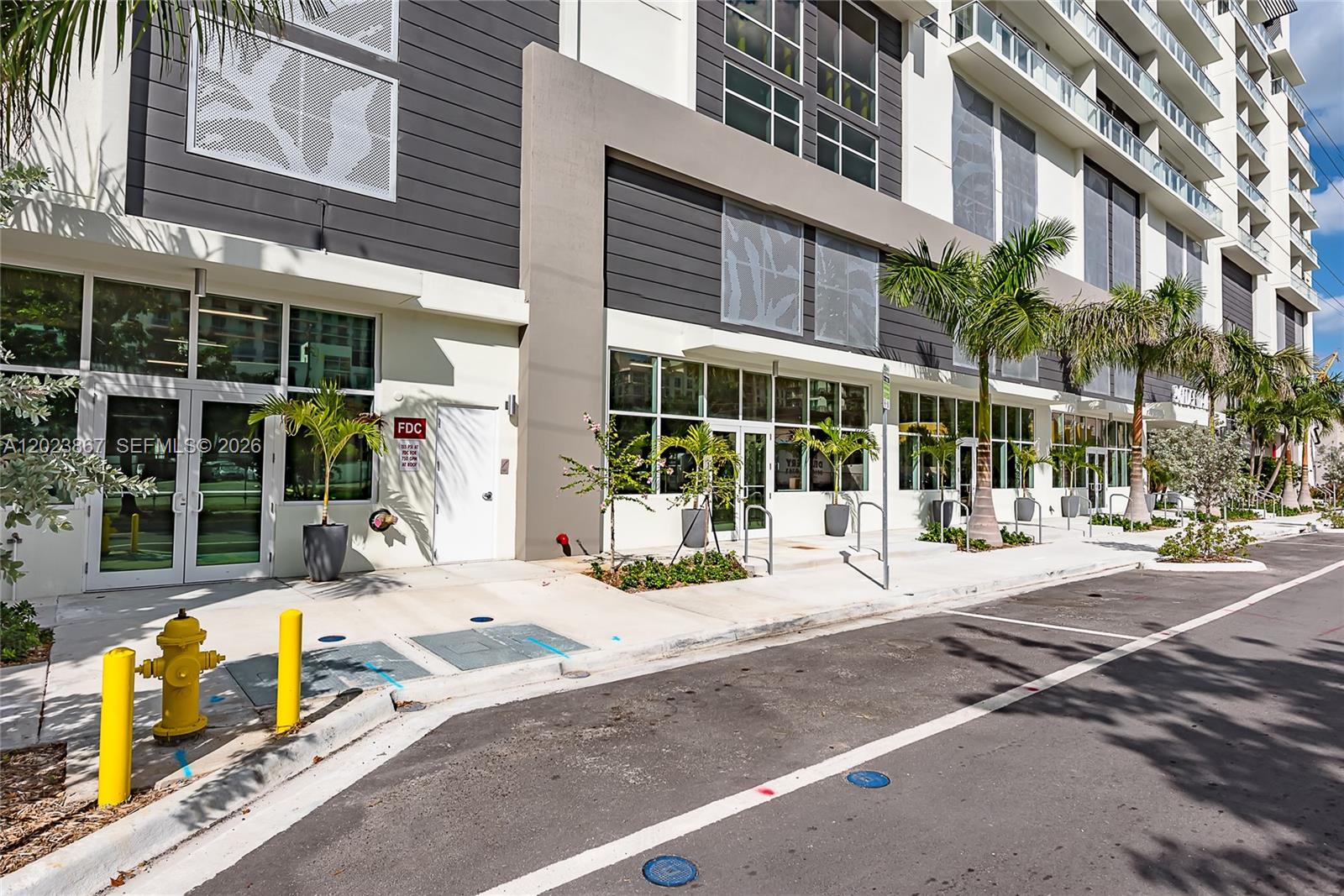 The exterior of a modern multi-story building features glass storefronts, a fire hydrant, and palm trees — 321 NE 26th St # 604, Miami FL 33137, MIAMI, FL