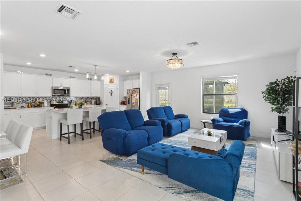 An open-concept living room and kitchen featuring blue furniture, white cabinetry, and tile flooring — 6018 Henderson Way, West Palm Beach FL 33415, WEST PALM BEACH, FL