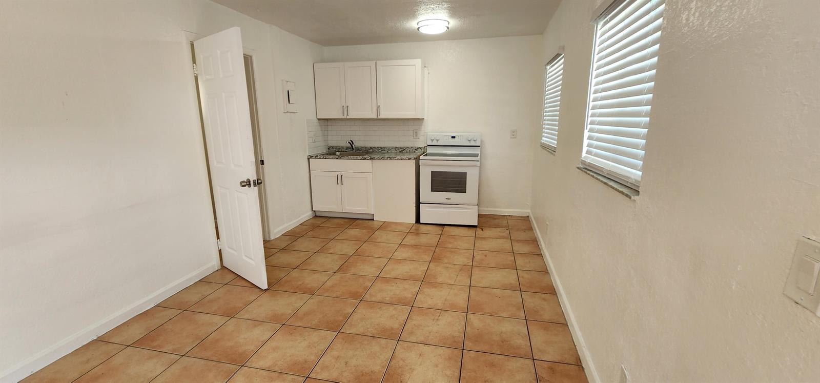 A small kitchen features white cabinets, a white stove, and light brown tile flooring — 620 NW 7th Avenue # 16, Pompano Beach FL 33060, POMPANO BEACH, FL
