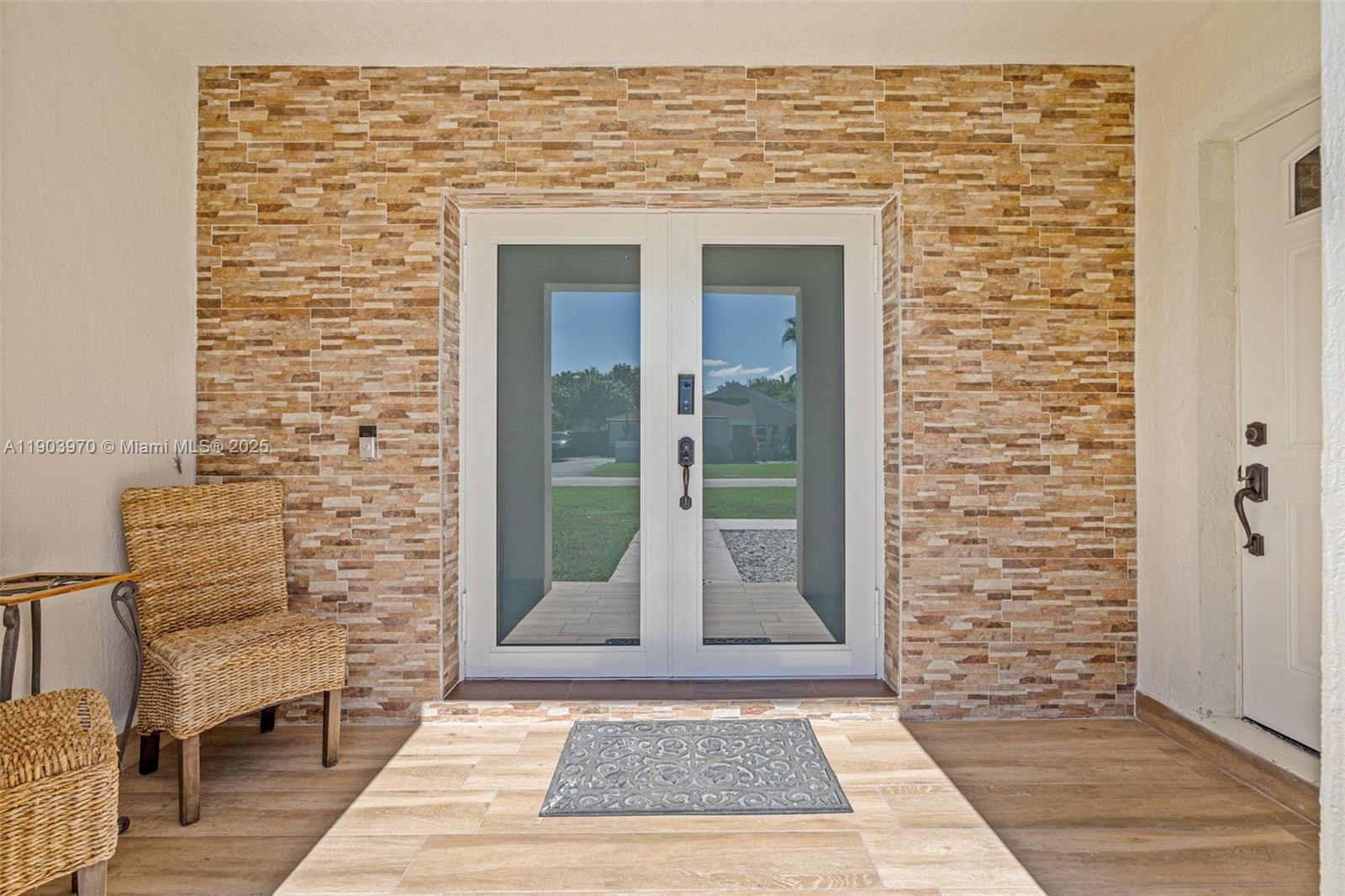 A stone-tiled accent wall frames a double glass door entrance with wicker chairs nearby — 15281 SW 153rd St, Miami FL 33187, MIAMI, FL