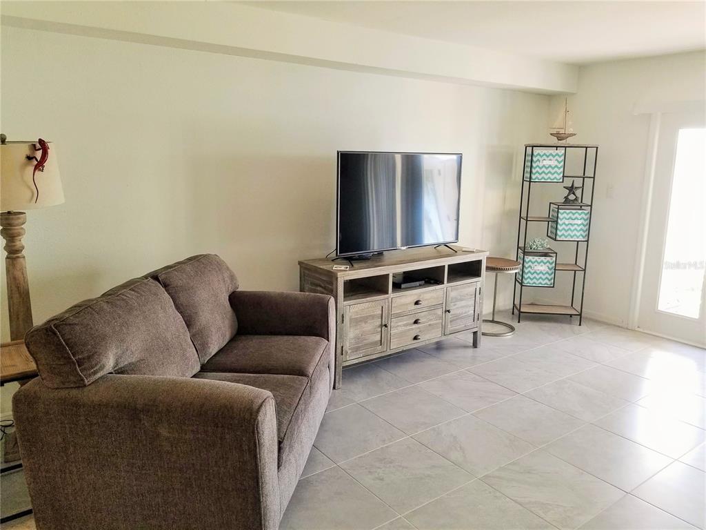 A living room features a gray sofa, a wooden media console, and a metal shelving unit — 169 POMPANO DRIVE SE, ST PETERSBURG, FL