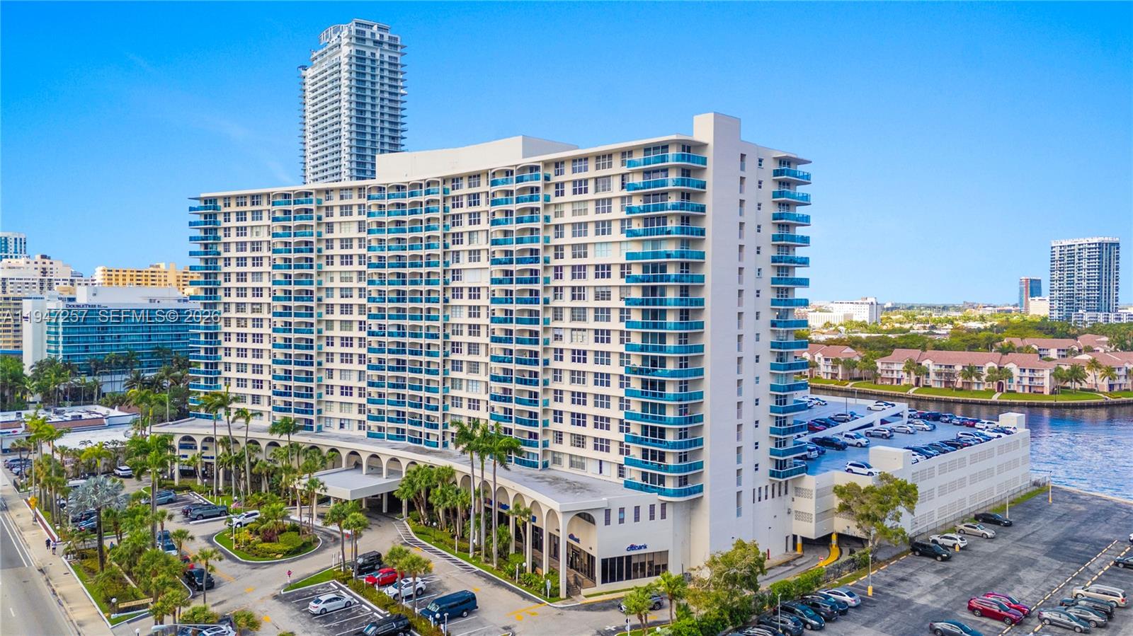 An aerial view of a large multi-story residential building with blue balconies and parking lots — 3800 S Ocean Dr # 419, Hollywood FL 33019, HOLLYWOOD, FL