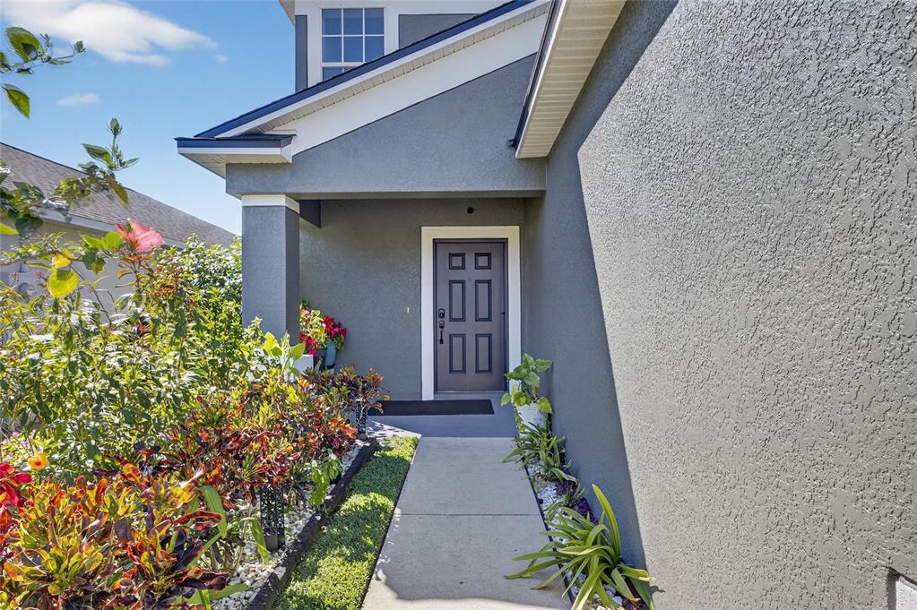 A concrete walkway leads to the front entrance of a gray house with landscaping — 1504 TRAILWATER STREET, RUSKIN, FL