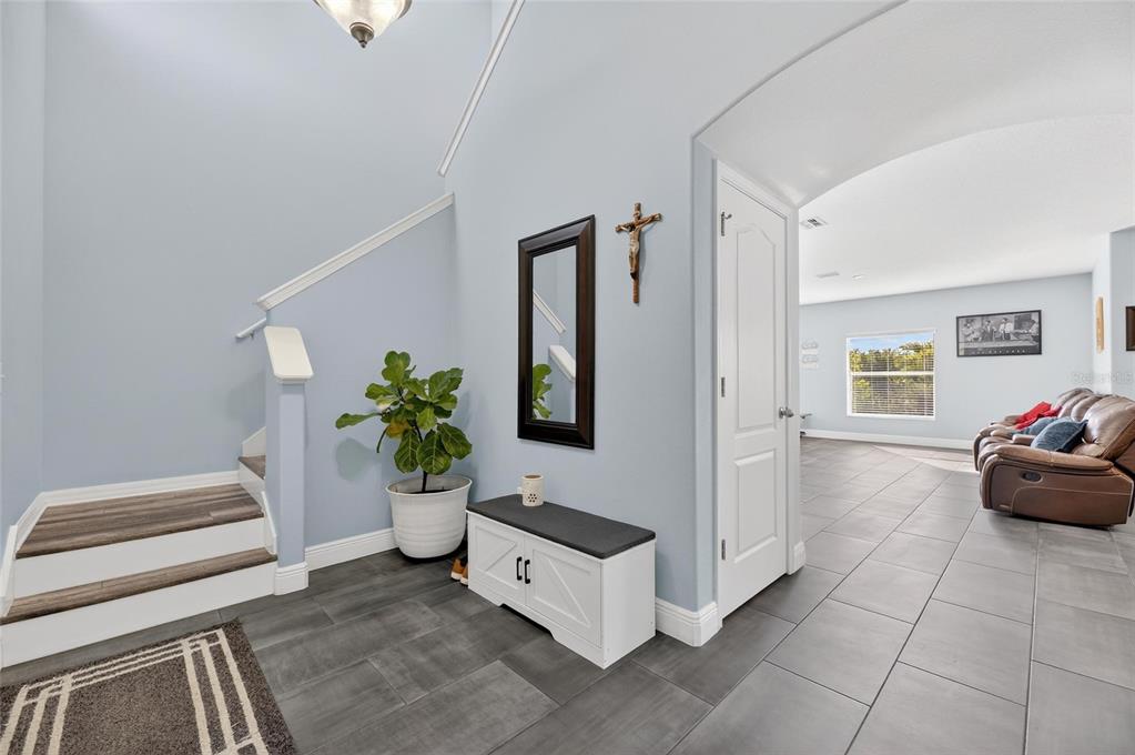 An entryway features light blue walls, gray tile flooring, a staircase, and a storage bench — 1504 TRAILWATER STREET, RUSKIN, FL