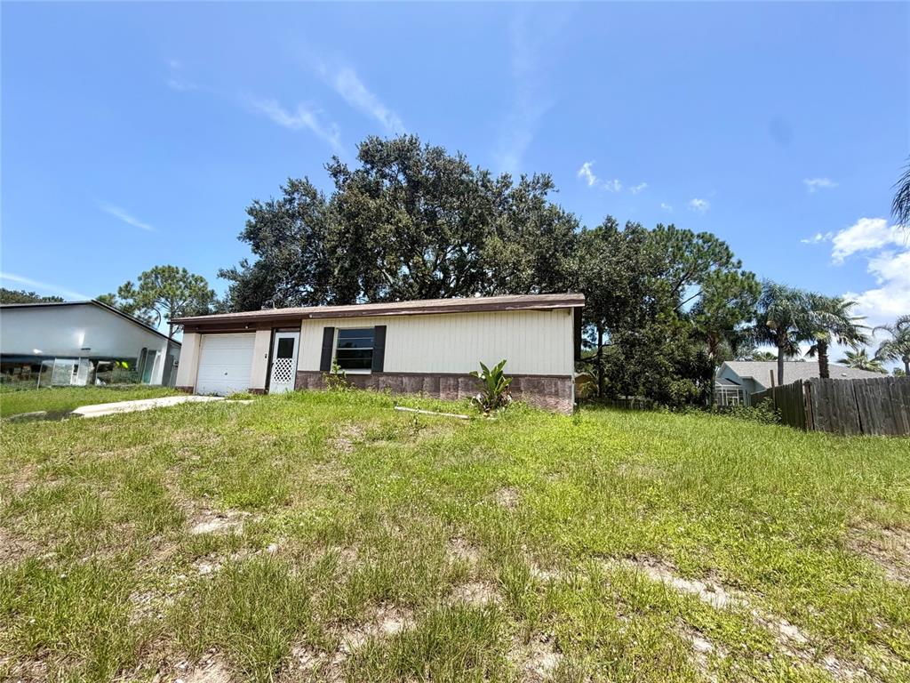 A single-story house with light siding and a stone-textured base sits on a grassy lot — 1306 DUKES DRIVE, TARPON SPRINGS, FL