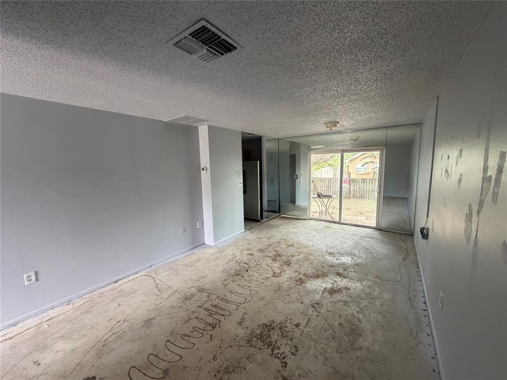 An empty room with gray walls, a concrete floor, and a sliding glass door — 1306 DUKES DRIVE, TARPON SPRINGS, FL