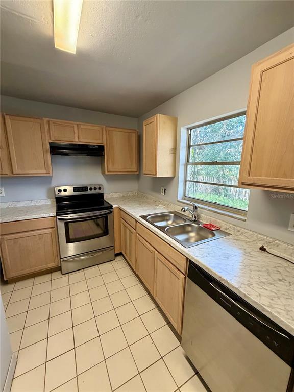 A kitchen features light wood cabinets, stainless steel appliances, and white tiled flooring — 1306 DUKES DRIVE, TARPON SPRINGS, FL