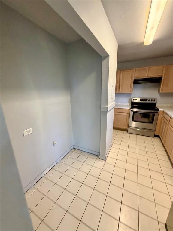 A kitchen features light-colored tile flooring, wooden cabinets, and a stainless steel oven — 1306 DUKES DRIVE, TARPON SPRINGS, FL
